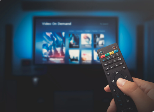 Pessoa usando o controle remoto diante da TV com serviço de vídeo sob demanda